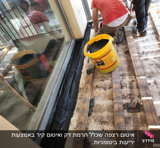 שני פועלים מתקנים רצפה עם דלי וחומר איטום
